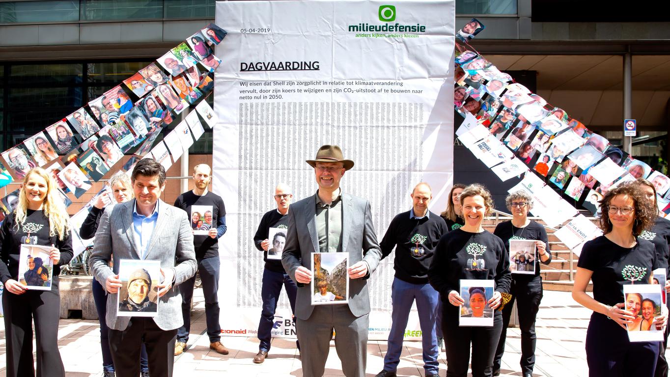 People stand in front of the court, holding photos of people who are co-plaintiffs in the court case against Shell in the Netherlands. 